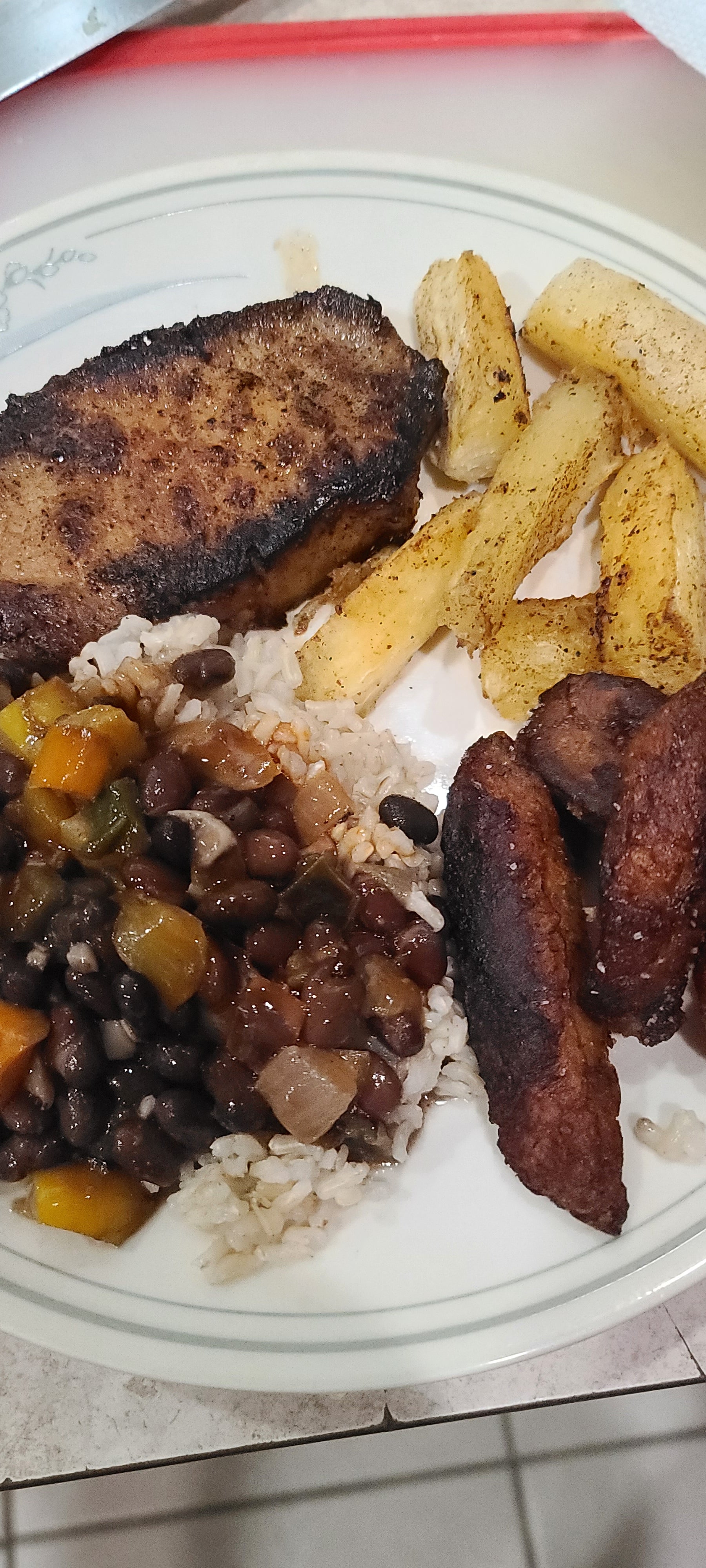 Plated meal with pork, beans, rice, and yucca fries on a white plate.