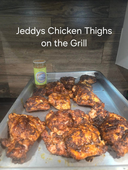Grilled chicken thighs on a tray with a jar of jeddys seasoning in front of a wooden wall.